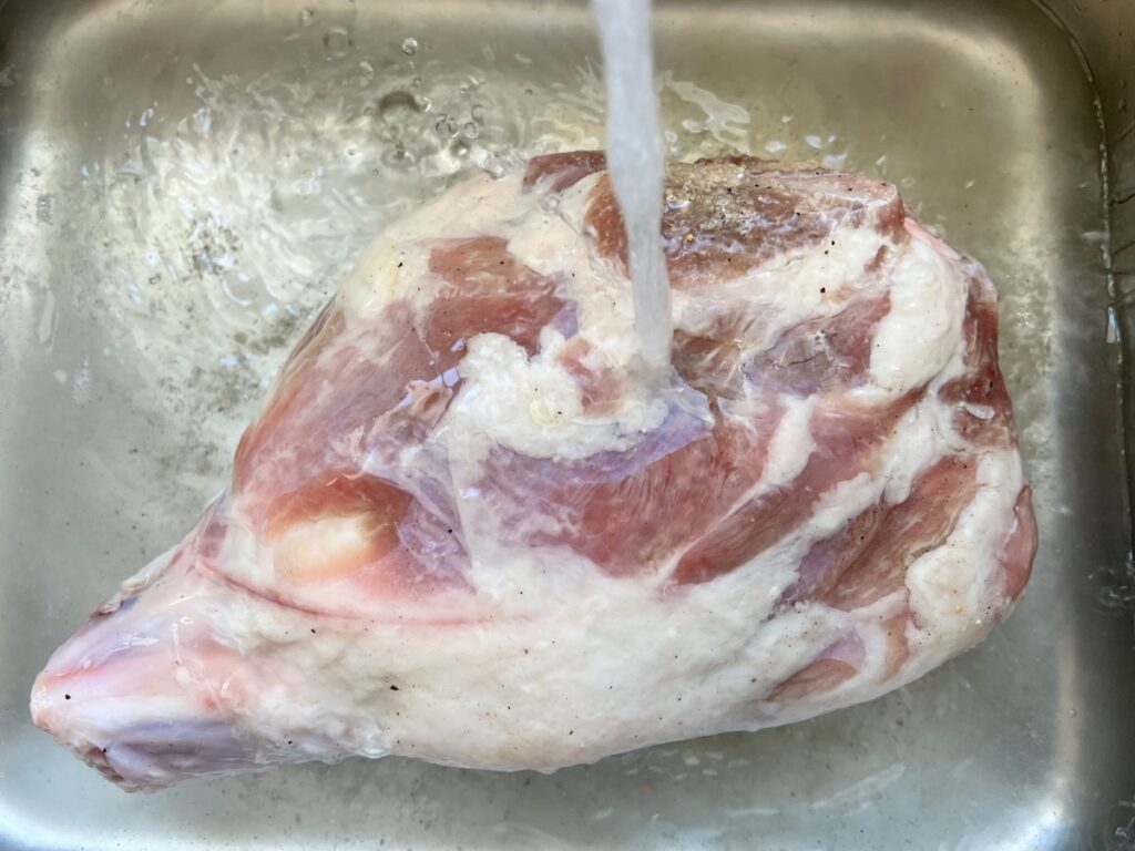 Water running in sink over pork shoulder to rinse off the brine.