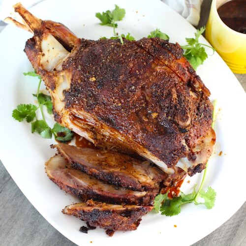 Whole roasted pork shoulder on the bone on a platter with some of it sliced for the Pork shoulder brine recipe.