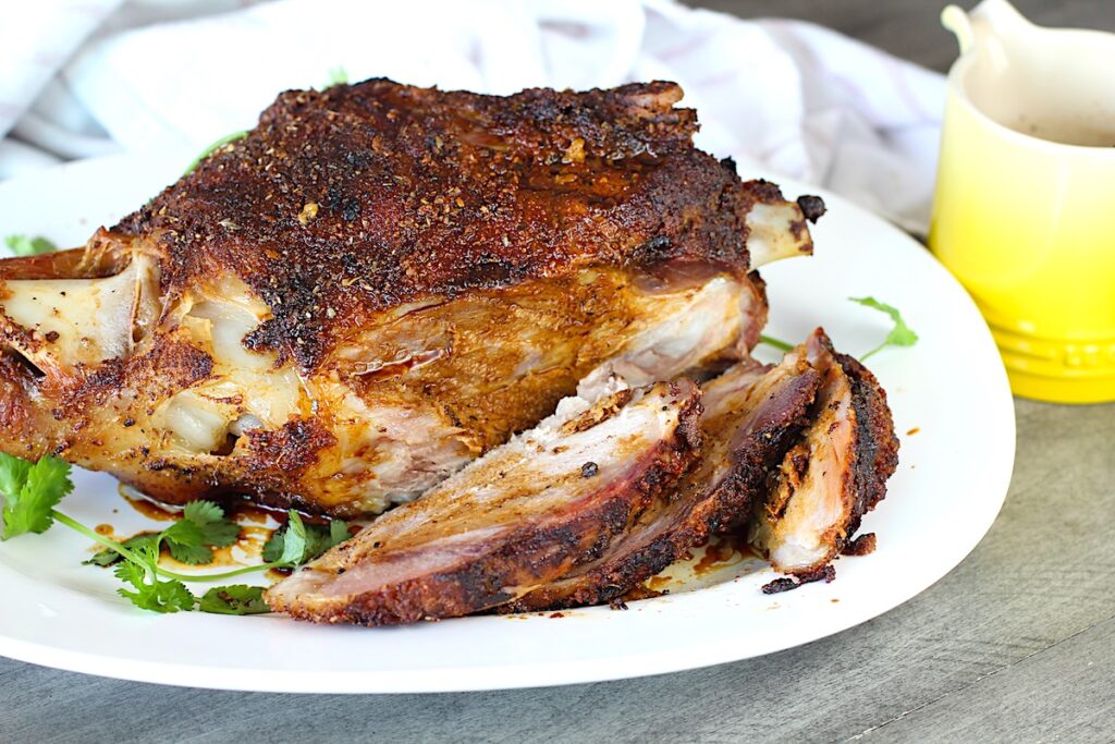Whole roasted pork shoulder on the bone on a platter with some of it sliced for the Pork shoulder brine recipe.