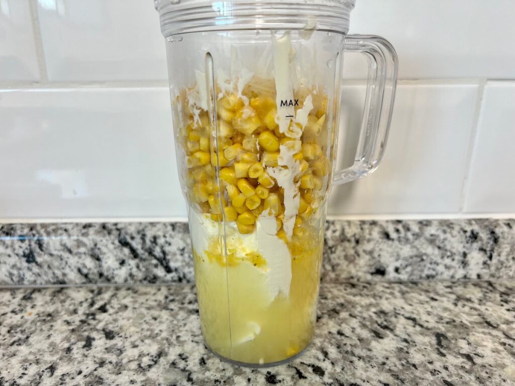 Blender filled with broth, cream cheese, and corn before blending for Corn Casserole Recipe with Cream Cheese.
