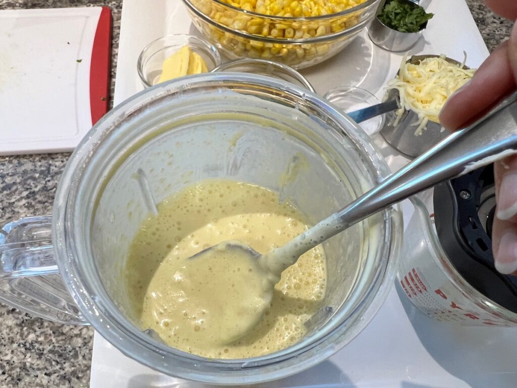 Spoon in blender to look at consistency of blended broth, cream cheese, and corn for Corn Casserole Recipe with Cream Cheese.