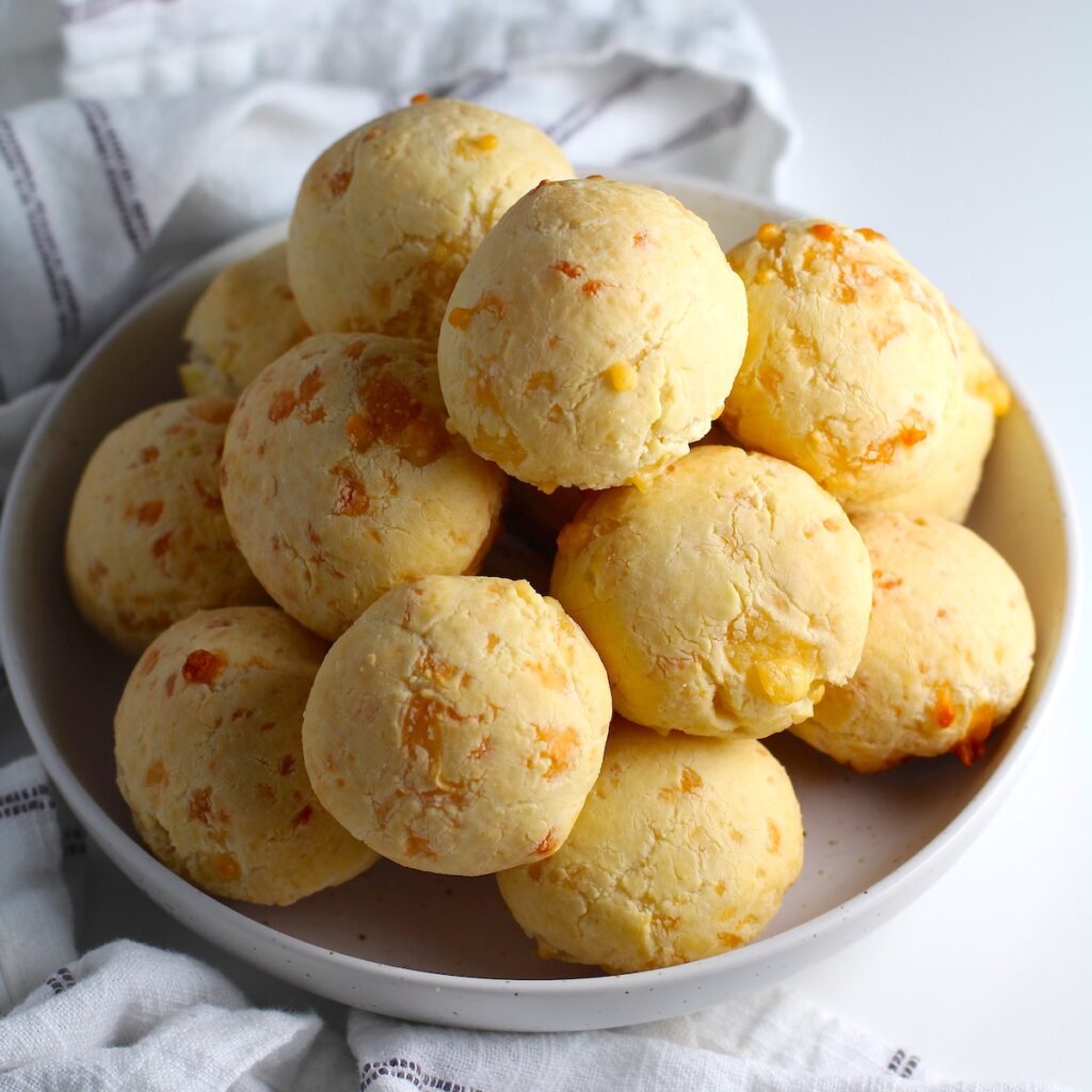 Bowl of golden Gluten Free Brazilian Cheese bread, or Pao de Queijo, stacked on top of each other.