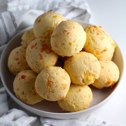 Bowl of golden Gluten Free Brazilian Cheese bread, or Pao de Queijo, stacked on top of each other.