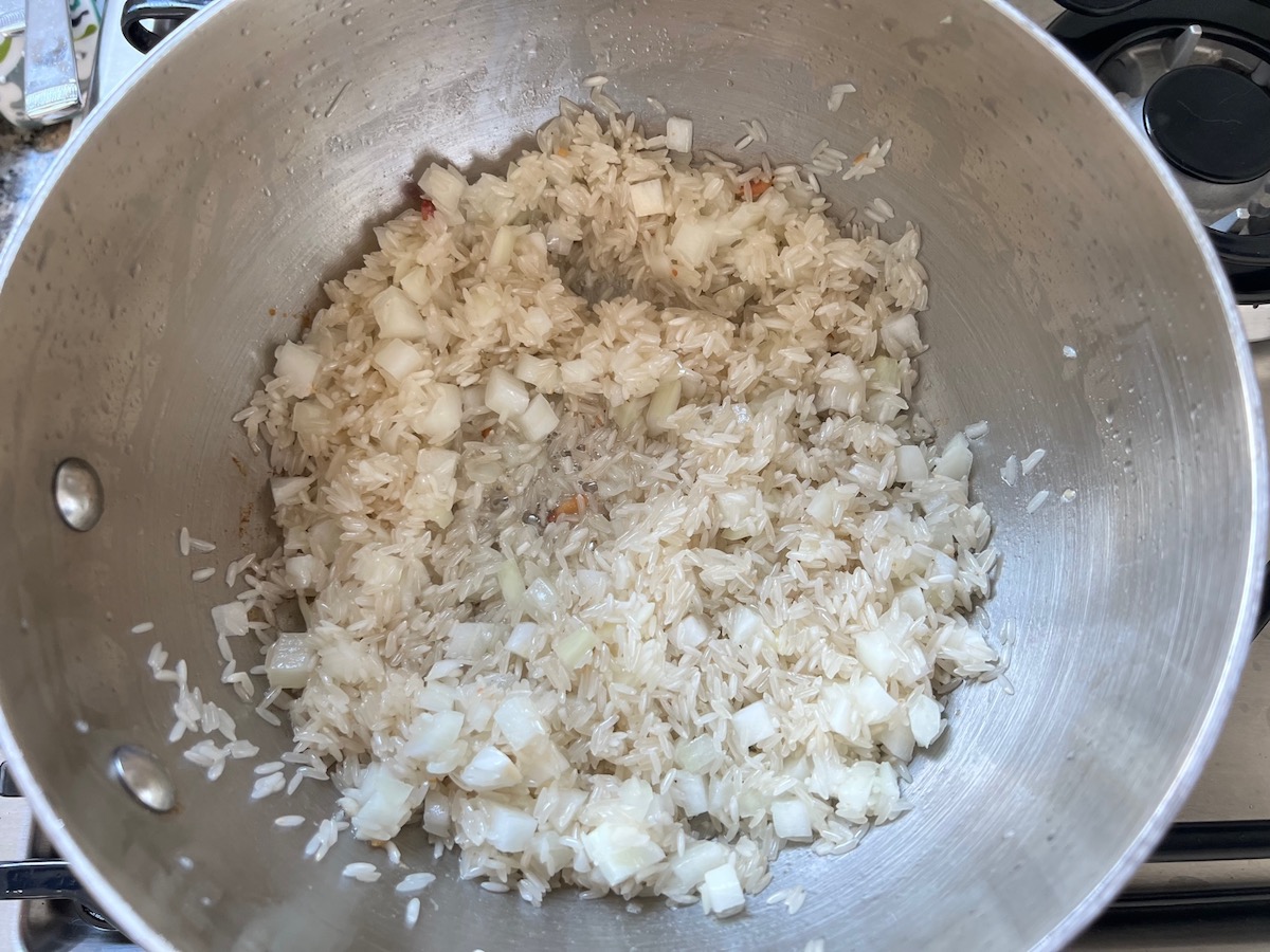 Uncooked rice and onions cooking in bacon fat for Arroz Pilaf.