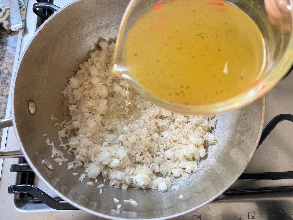 Pouring broth over rice and onions in pot for Arroz Pilaf.