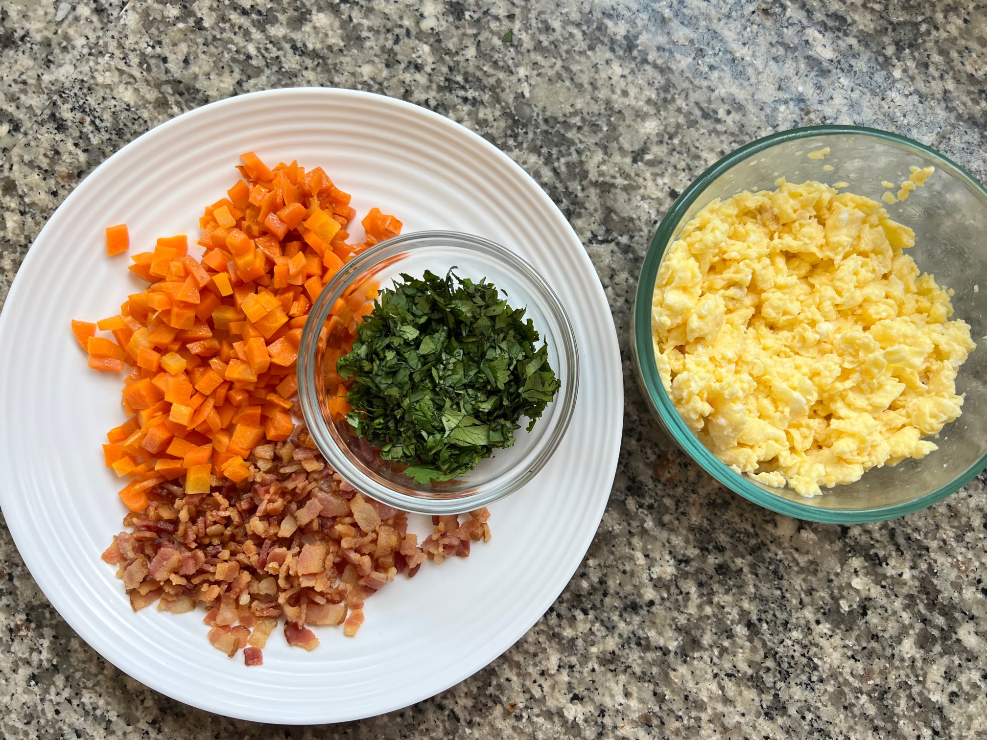 Cooked diced carrots, crisp bacon bits, chopped cilantro, and scrambled eggs on plates and bowls for Arroz Pilaf.