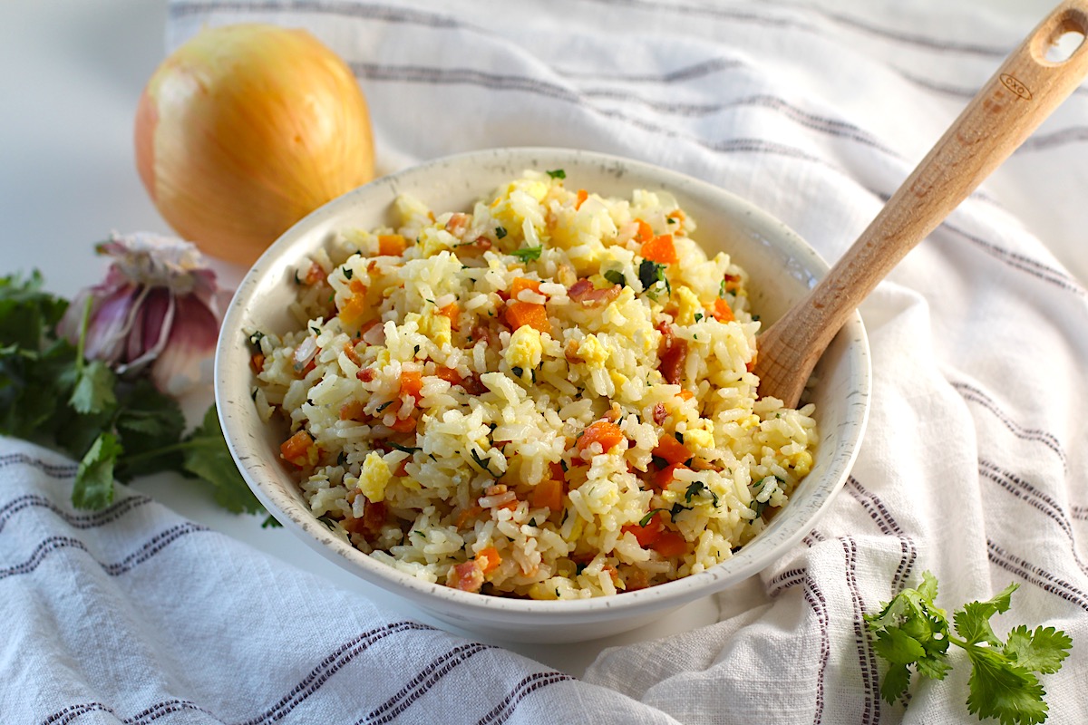 Arroz pilaf in a bowl with carrots, bacon, and cilantro mixed in and a spoon in the bowl.
