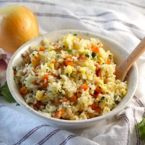 Arroz pilaf in a bowl with carrots, bacon, and cilantro mixed in and a spoon in the bowl.