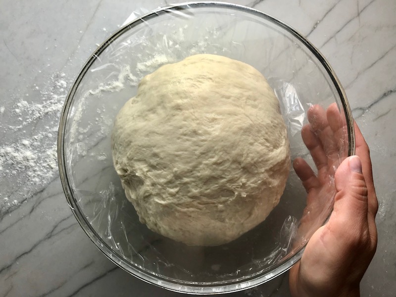Brazilian Pizza dough in a glass bowl covered with plastic wrap for rising..