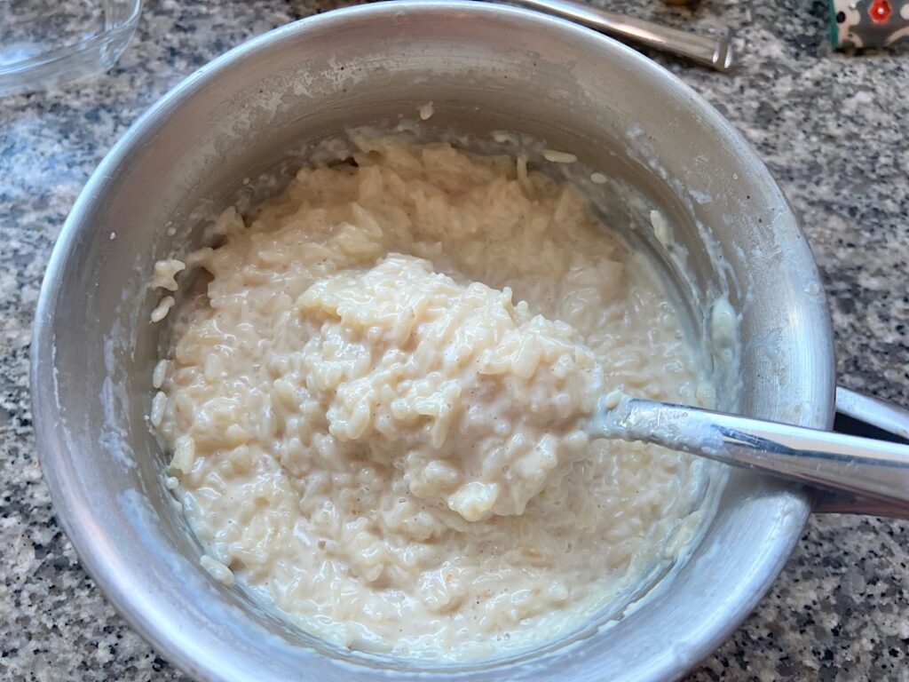 Spoon stirring thickening Rice Pudding with condensed milk in a pot on stove.