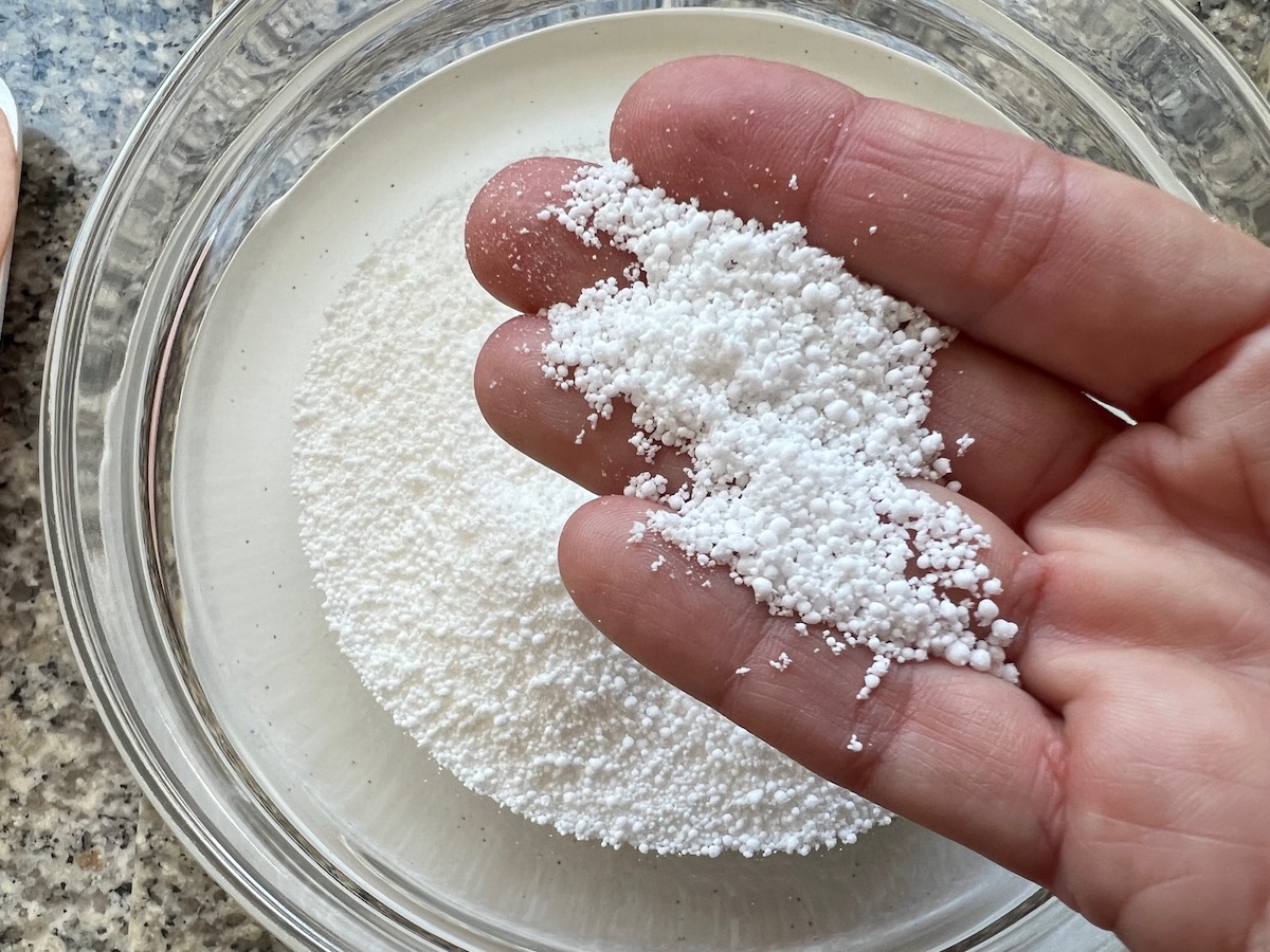 Hand holding tapioca starch pearls over a bowl of tapioca starch for Brazilian breakfast tapioca recipe.