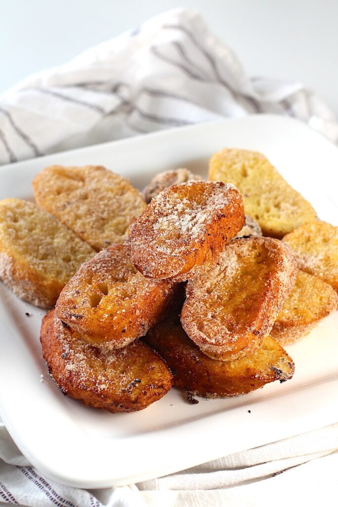 Slices of Brazilian French Toast with condensed milk fried golden brown and dusted with cinnamon sugar stacked on a plate.