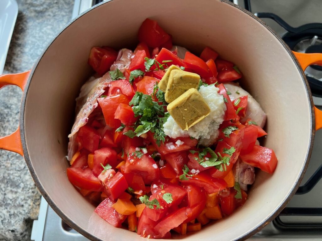 Three bouillon cubes, minced garlic, chopped parsley, and chopped fresh tomatoes added to pot with raw chicken for the Canja Brazilian Chicken and Rice Soup recipe.