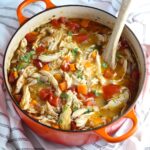 Canja Chicken Rice Soup in a pot with carrots and tomatoes and parsley and a wooden spoon on counter.