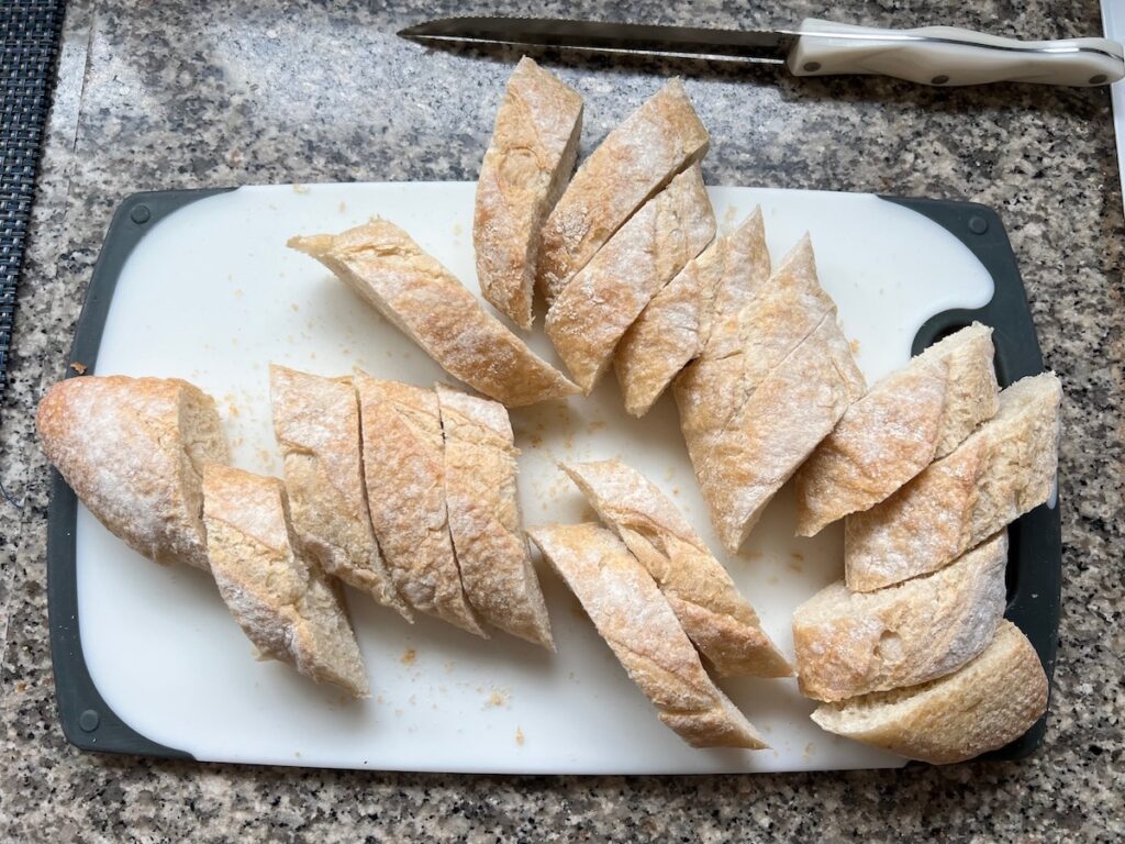 One-inch slices of baguette on a cutting board on counter for Brazilian French Bread with Condensed Milk recipe.