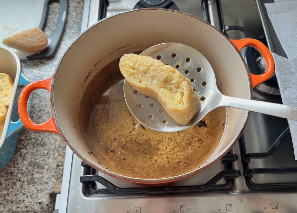 Slotted large flat spoon holding an egg-coated slice of bread over hot oil in pot for Brazilian French Toast with Condensed Milk.