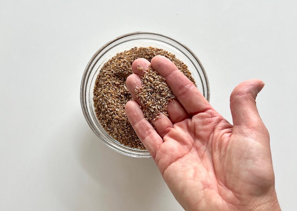 Hand holding dry bulgur wheat over a bowl with more on table for Kibe Mediterranean Ground Beef Kabab recipe.