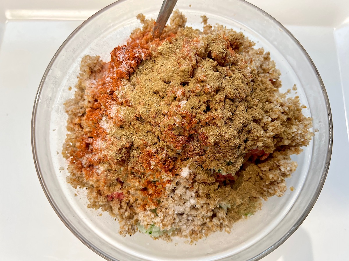 Bowl with raw ground beef, bulgur wheat, seasonings, and blended onions, garlic, and mint before being mixed for Kibe Mediterranean Ground Beef Kabab recipe.