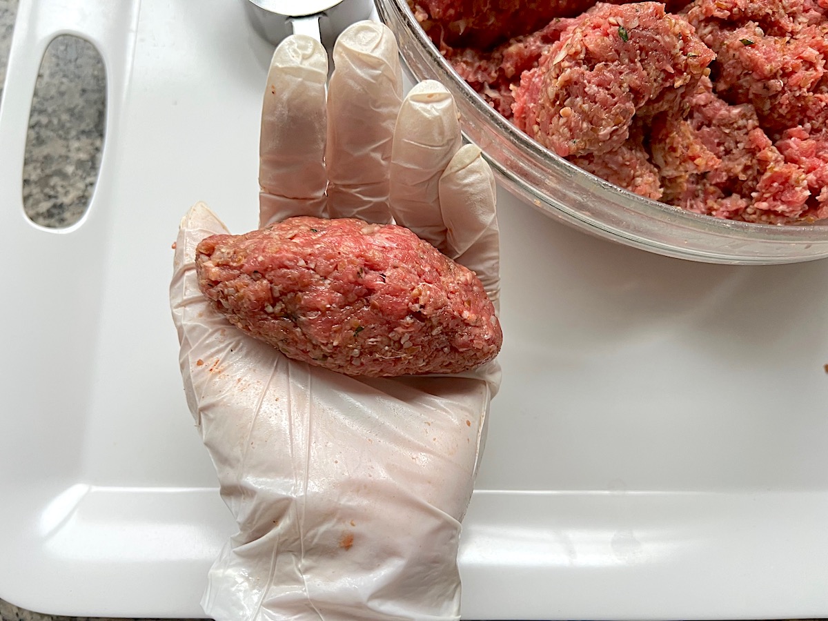 Ground beef mixture scooped up and shaped into a football shape in glove-covered hand for Kibe Mediterranean Ground Beef Kabab recipe.
