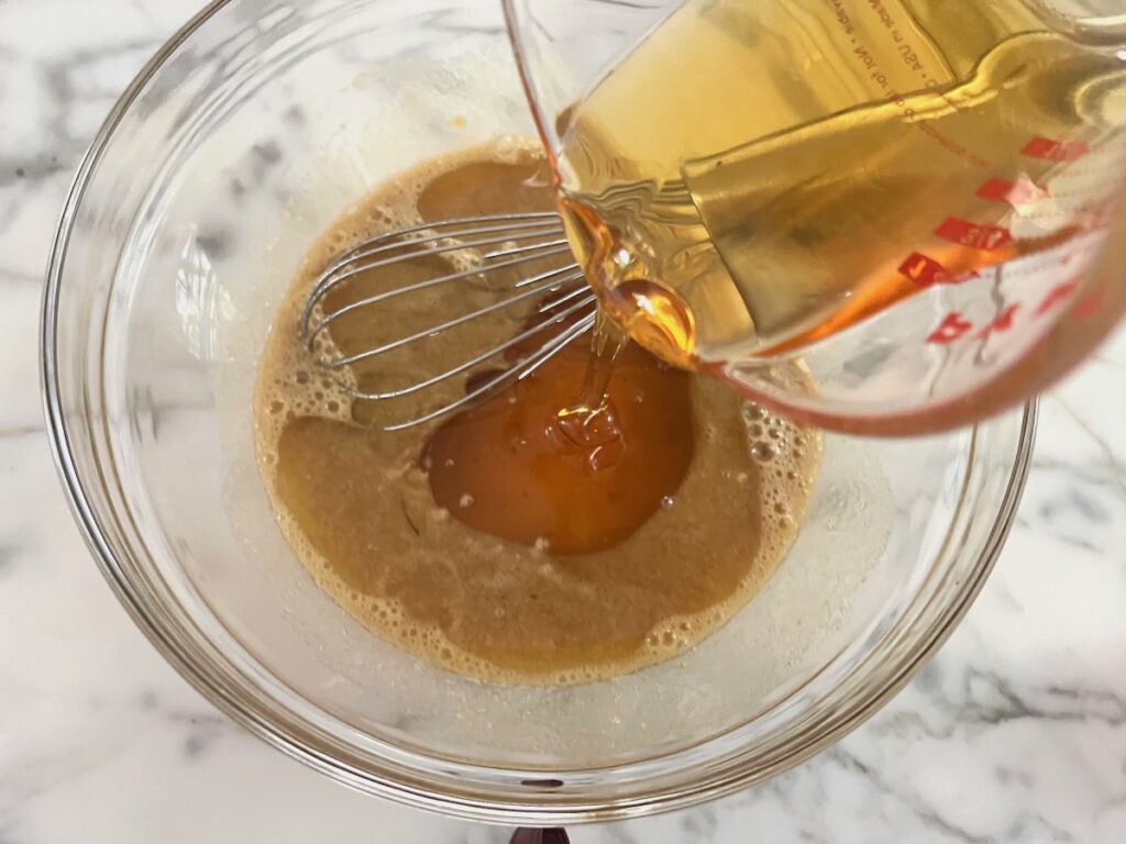 Honey being poured into sugar and eggs in a clear glass bowl before being mixed for the Pao de Mel recipe, Brazilian cakes filled with dolce de leite and covered with chocolate.
