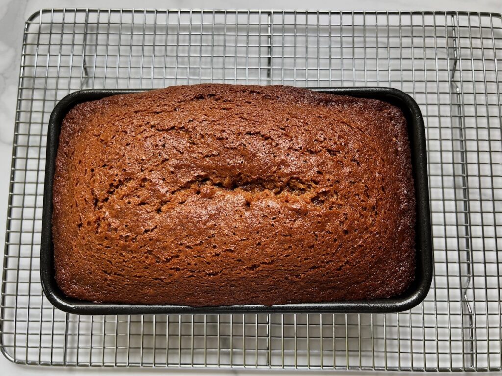 Fully baked and golden brown Honey Loaf in loaf pan on cooling rack.