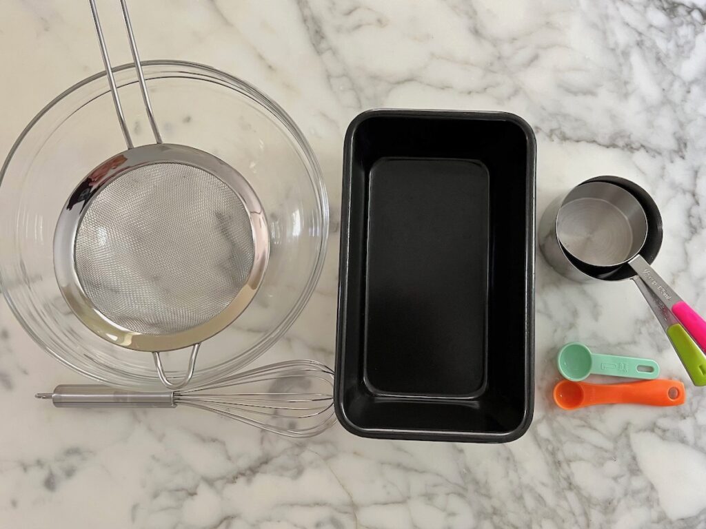 BOwl, whisk, loaf pan, measuring cups and spoons on counter for the Honey Loaf recipe.