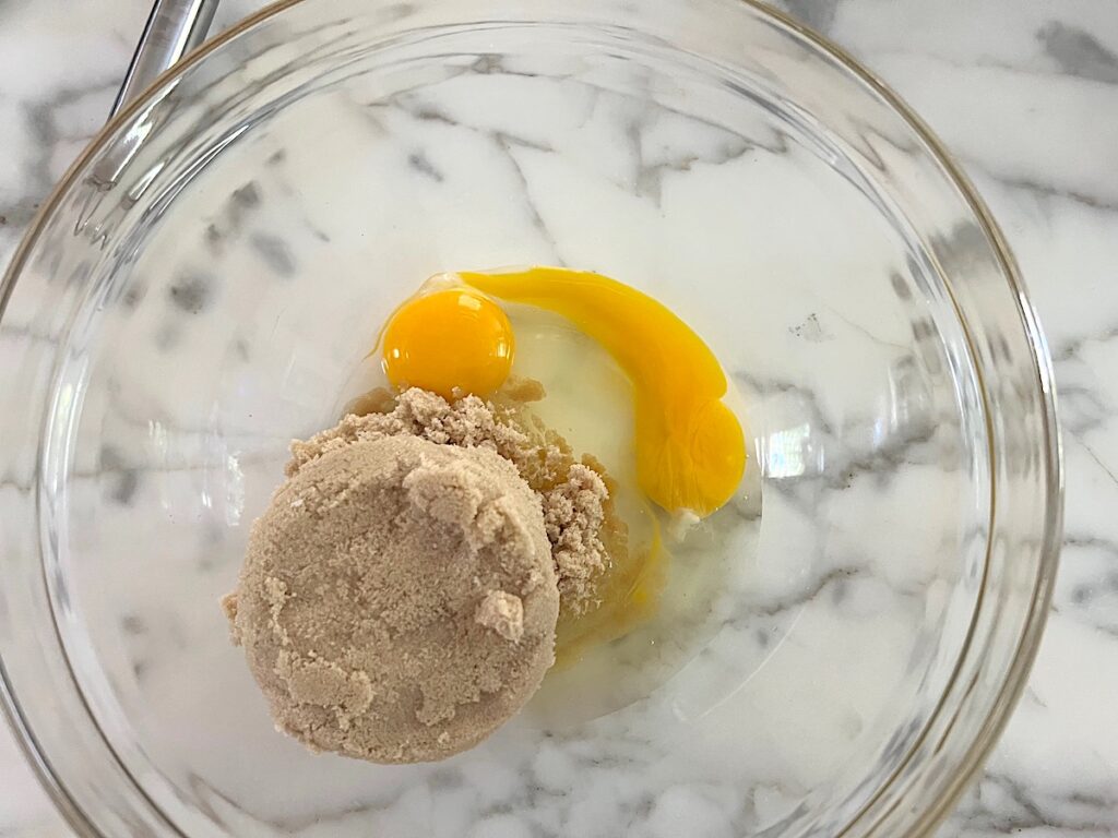Brown sugar and 2 eggs in a clear glass bowl before being mixed for the Honey Loaf recipe.
