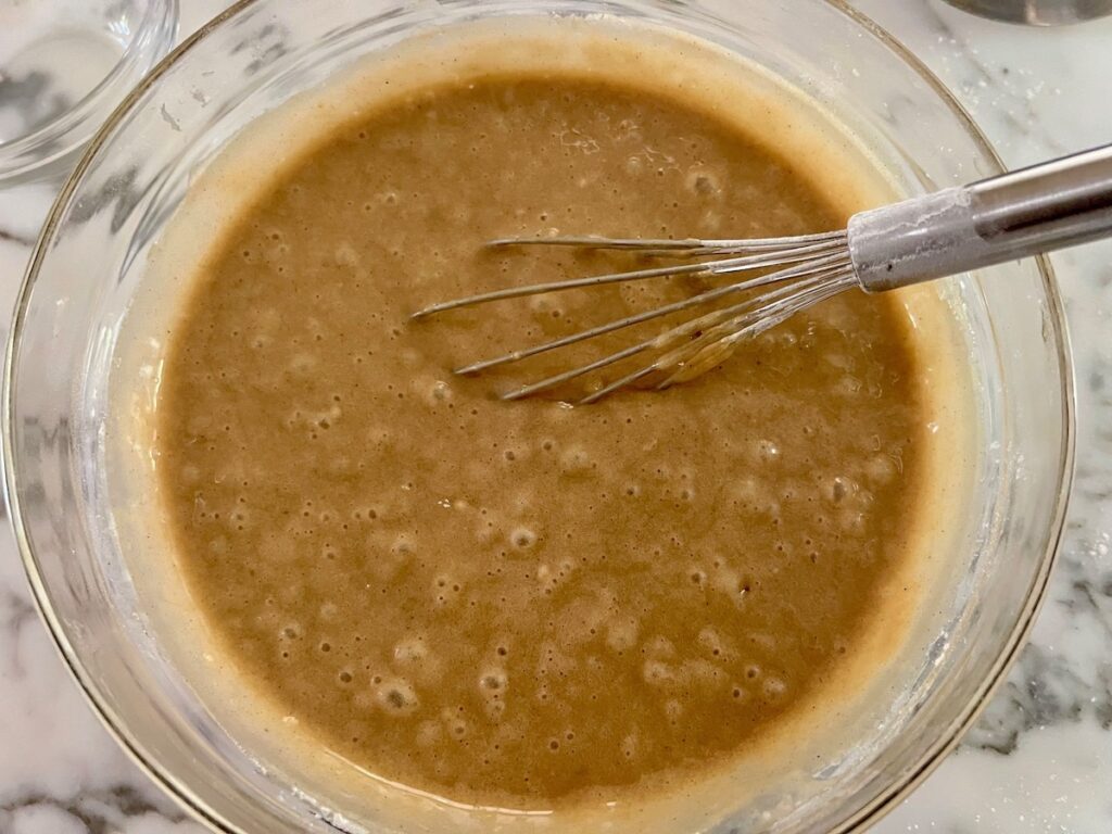 Finished brown batter with whisk in a clear glass bowl for the Honey Loaf recipe.