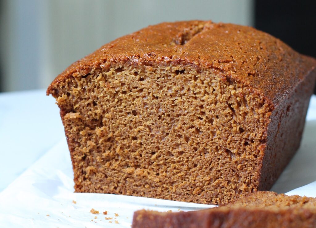 Honey Loaf cake baked beautifully golden brown on table with a slice in front showing the moist inside.
