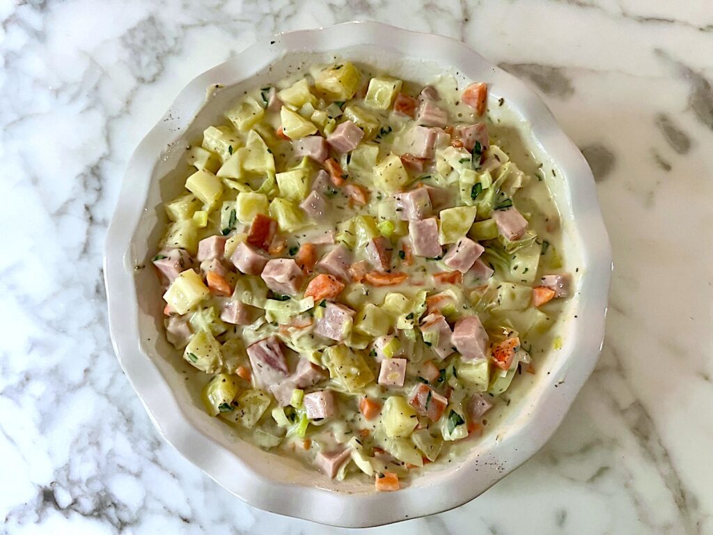 The prepared filling is added to a pie dish on a countertop for Ham and Leek Pie recipe.