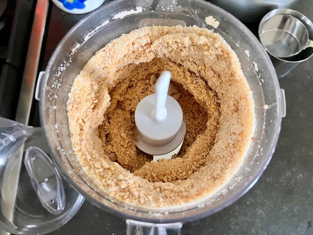 Roasted peanuts, granulated sugar, and salt in a food processor being blending for Brazilian Peanut Candy recipe (Pacoca).