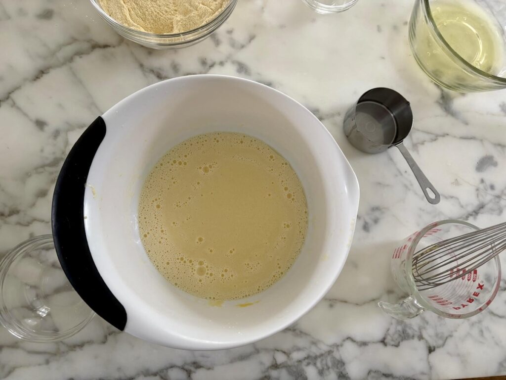 Sugar, egg yokes, and milk mixed in white bowl for this Bolo de Fuba, Cornmeal Cake, recipe.