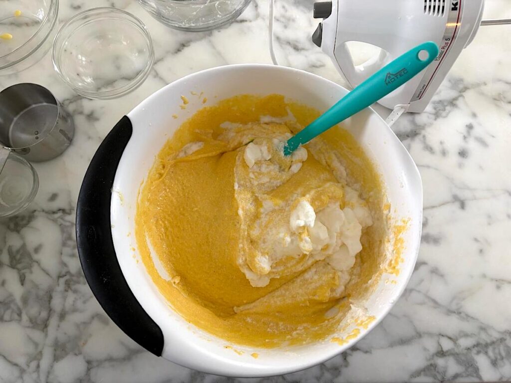 Blue spatula folding soft peak egg whites into the cornmeal batter for this Bolo de Fuba, Cornmeal Cake, recipe.