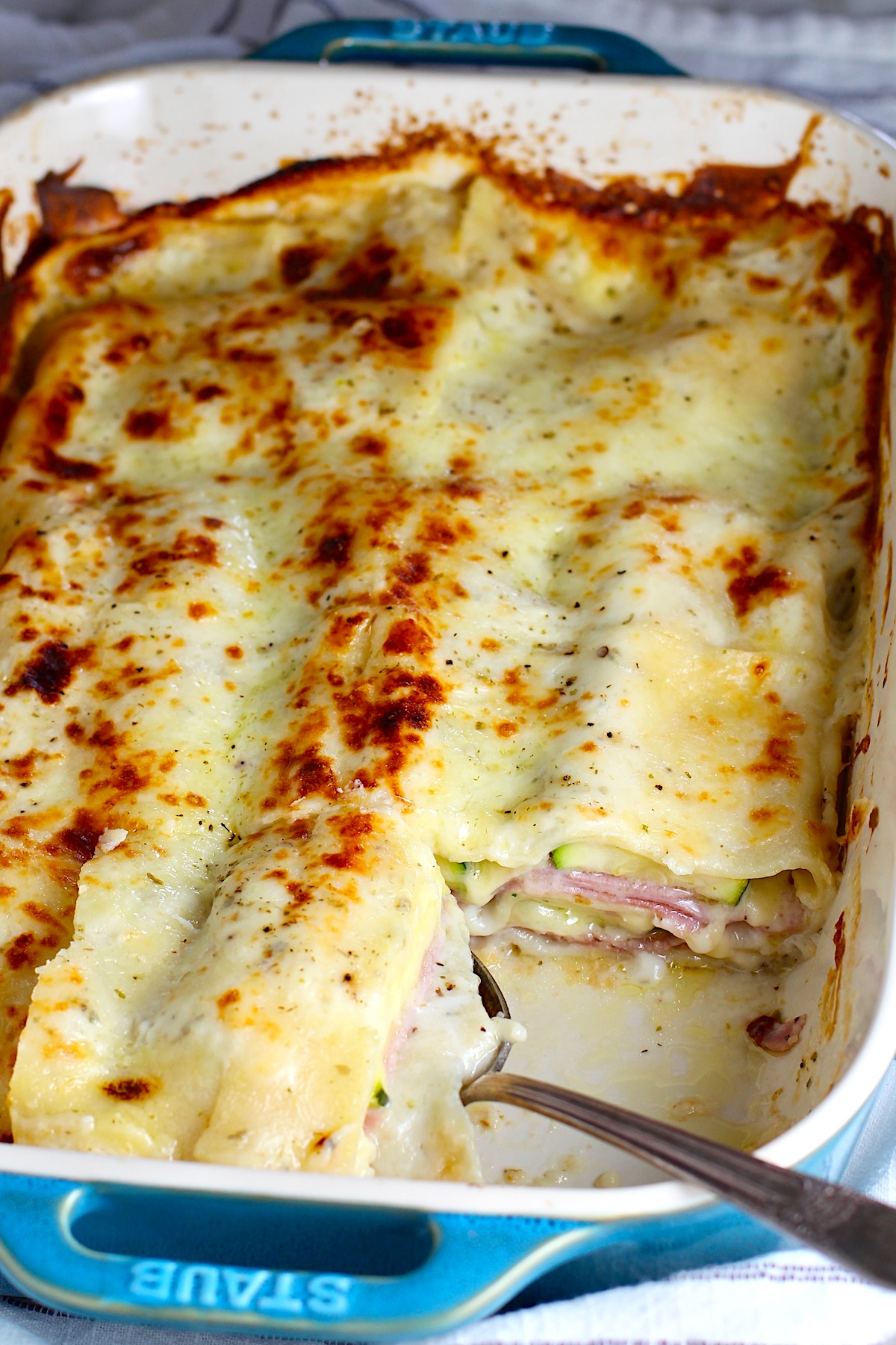 Bechamel Sauce Lasagna In a casserole dish with a piece taken out from corner and spoon in it's place.