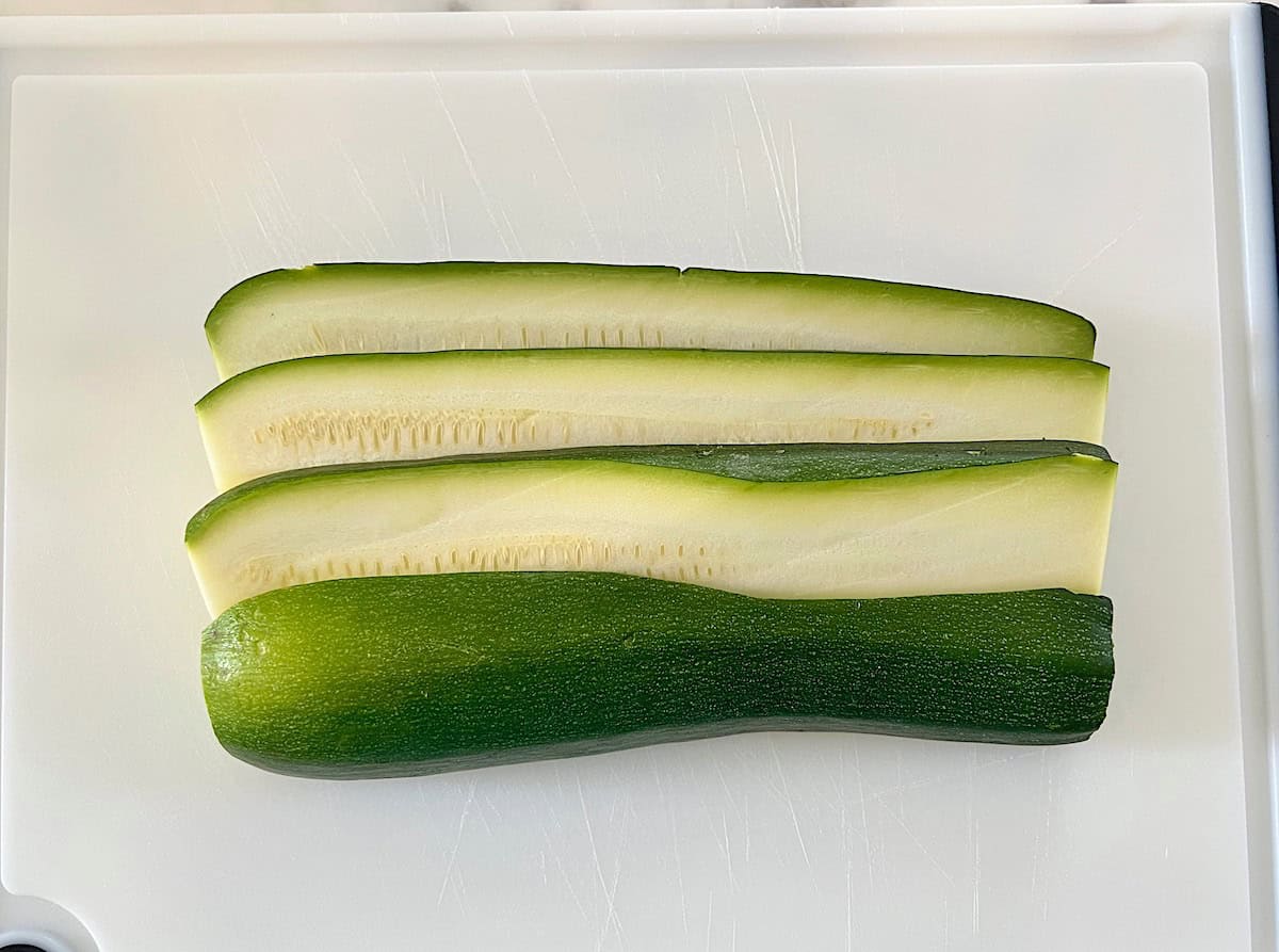 Fresh green Zucchini on a cutting board sliced into long ¼ inch thick strips from stem to stem for the Bechamel Sauce Lasagna recipe.