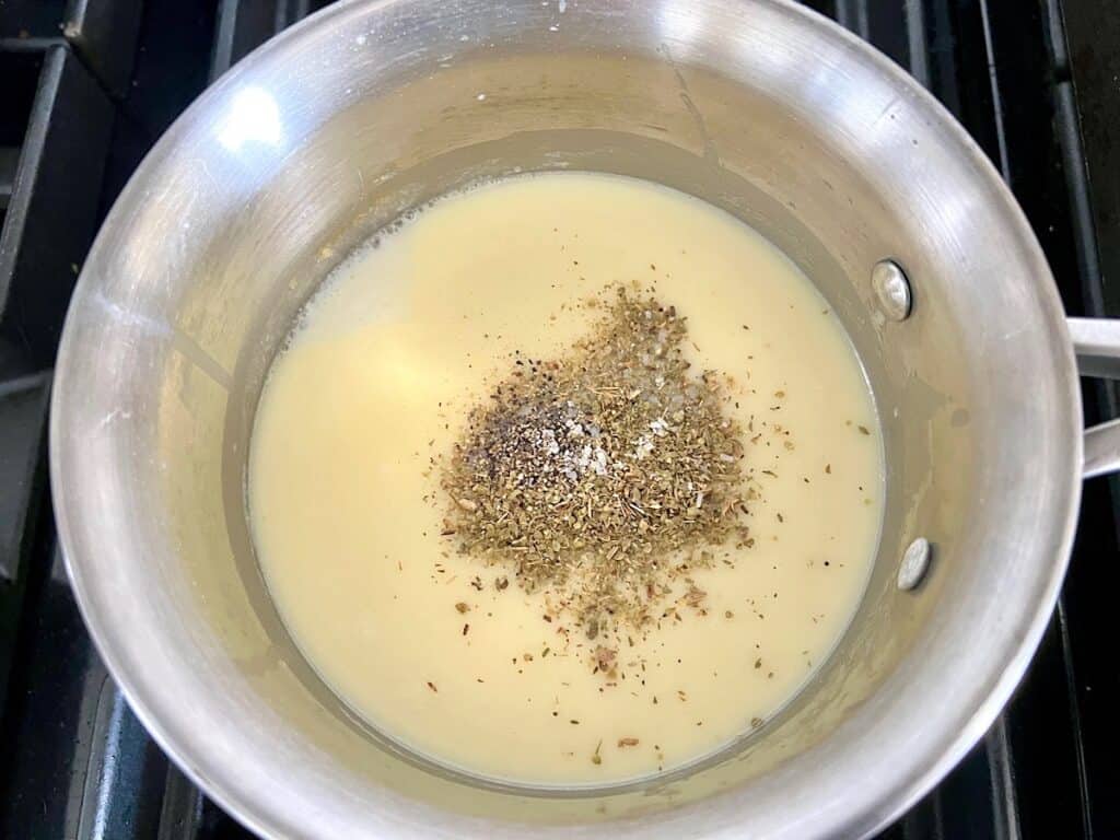 Seasonings added on top of bechamel sauce in a saucepan for Bechamel Sauce Lasagna.