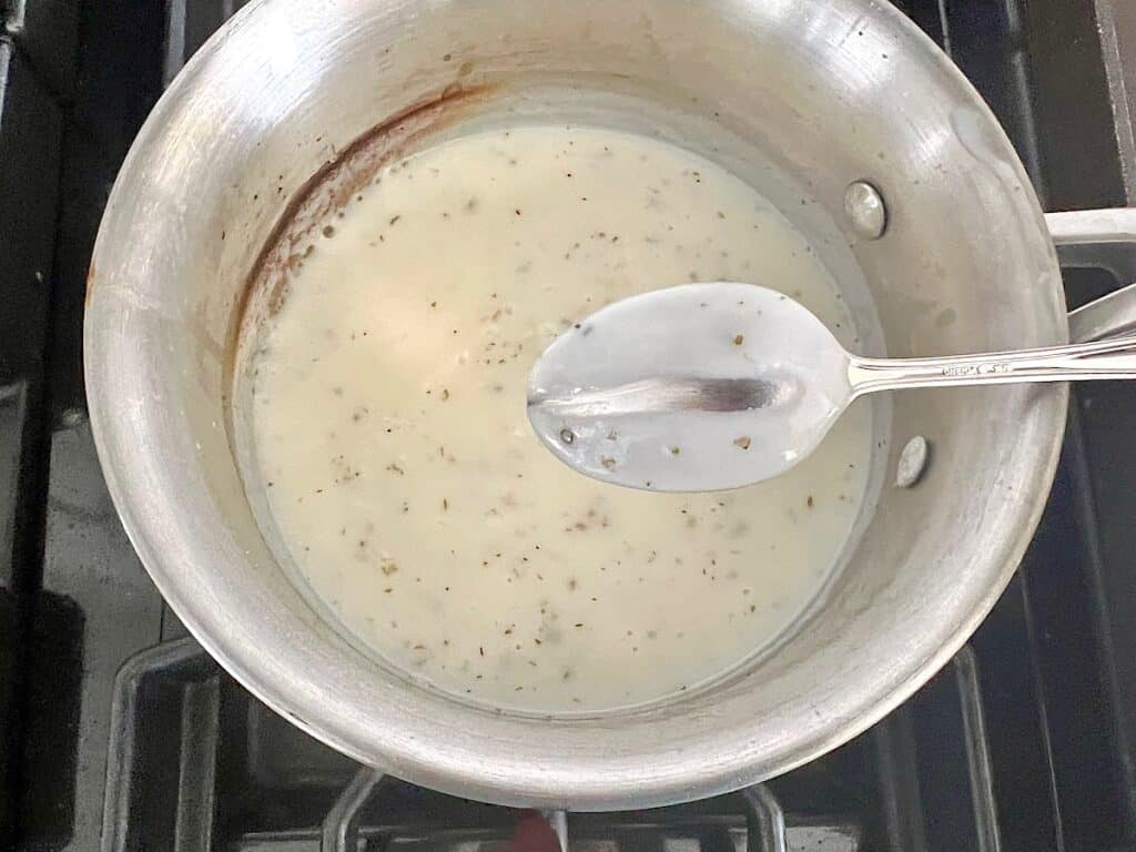 Spoon over saucepan with track wiped on back to show thickened bechamel sauce for Bechamel Sauce Lasagna.