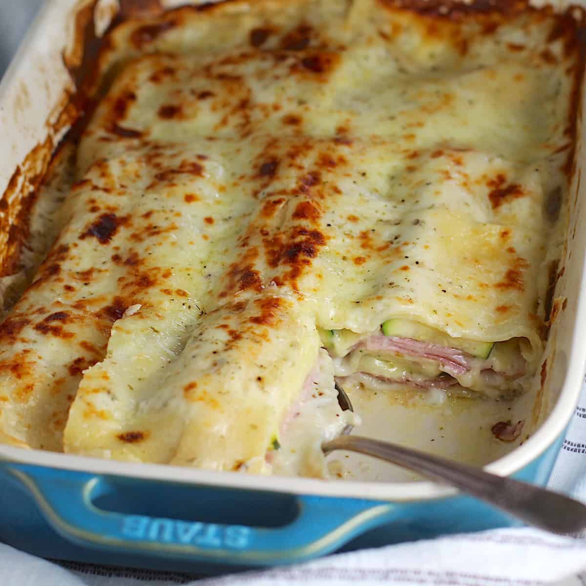 Bechamel Sauce Lasagna In a casserole dish with a piece taken out from corner and spoon in it's place.