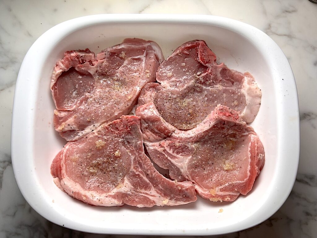Raw bone-in pork chops with lemon garlic marinade in a casserole dish for this Pork Chops with Onions recipe.
