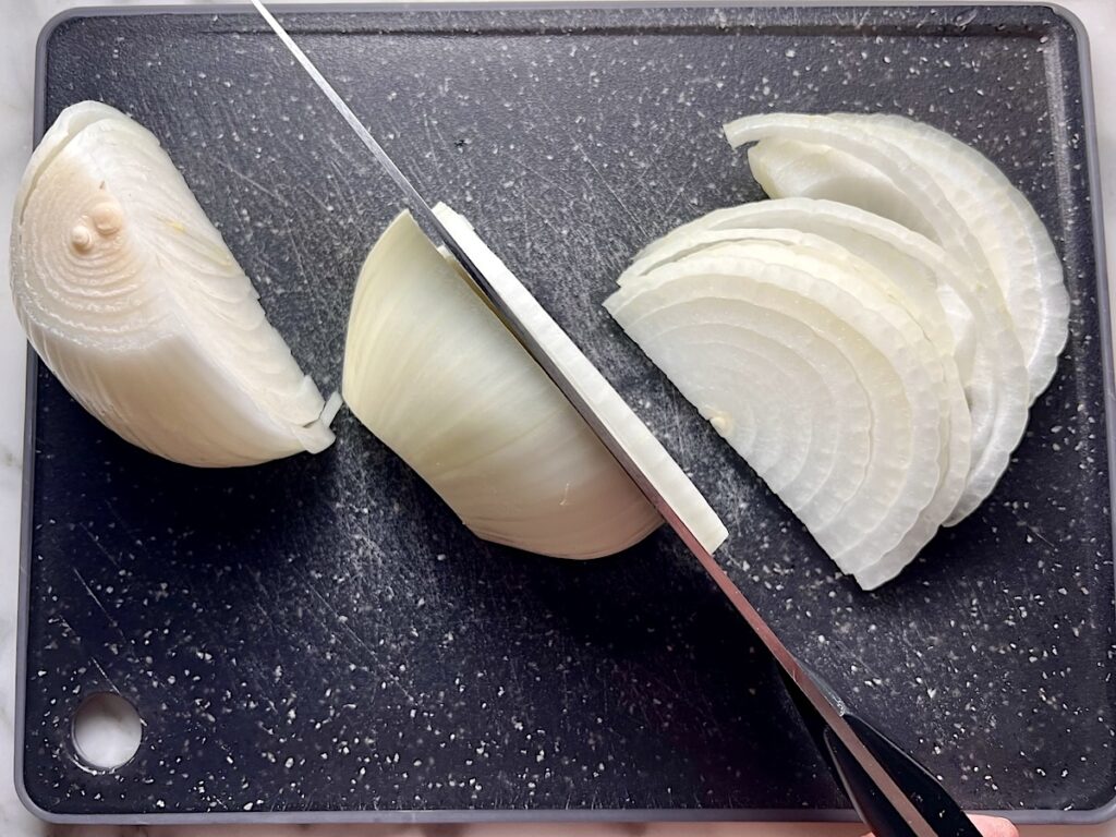Chefs knife slicing onions on a cutting board for this Pork Chops with Onions recipe.