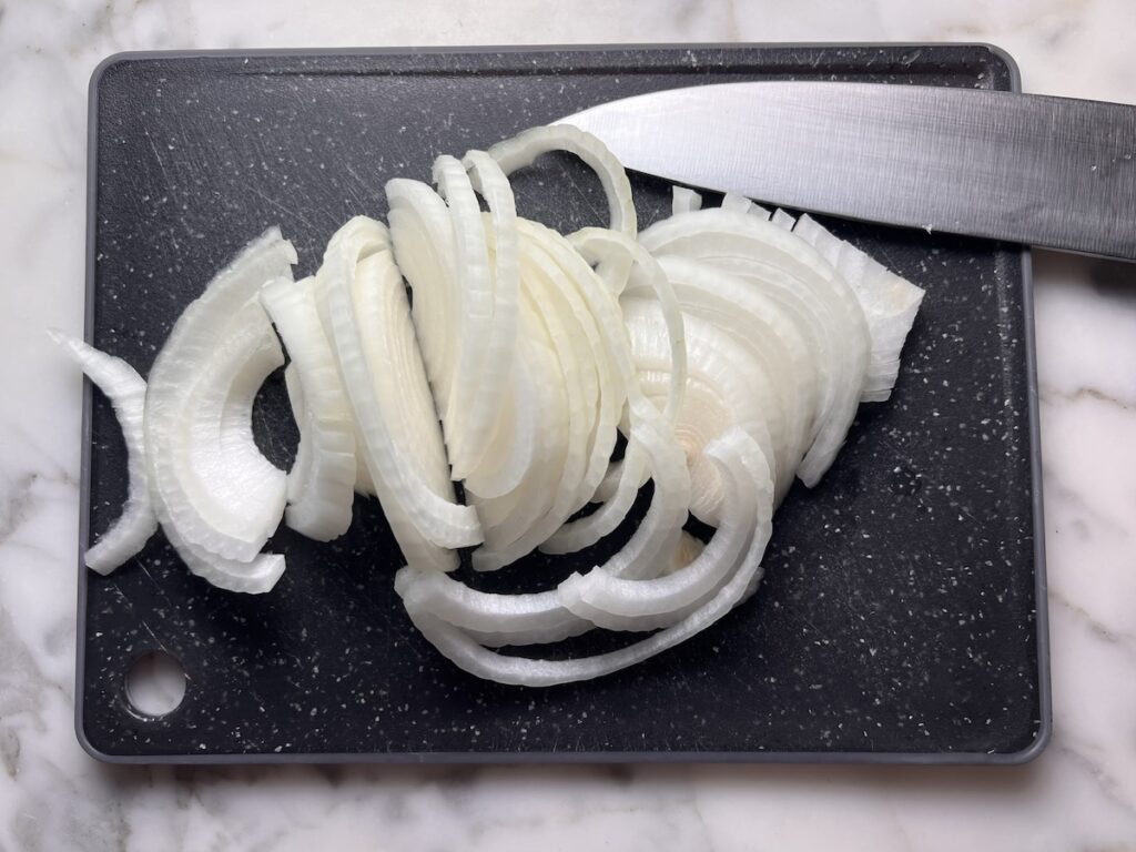 Sliced onions on a cutting board with chefs knife for this Pork Chops with Onions recipe.