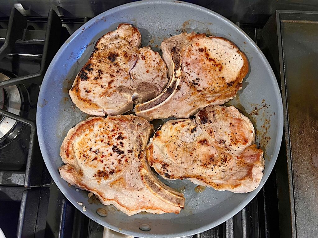 Bone-in pork chops browned on top in frying pan for this Pork Chops with Onions recipe.