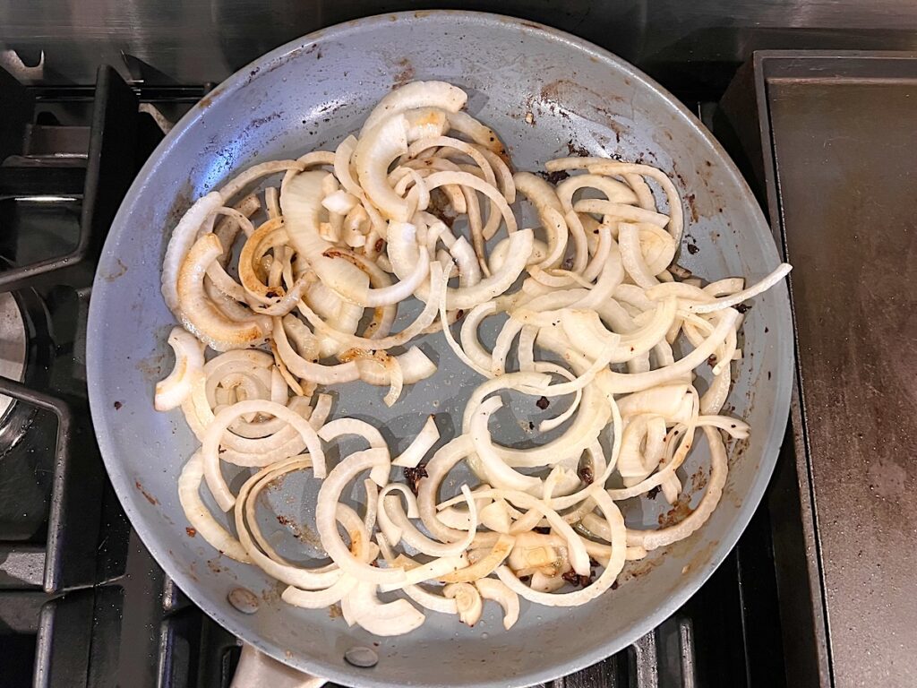 Sliced onions lightly browned and cooking in frying pan for this Pork Chops with Onions recipe.